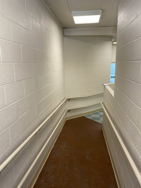 Empty narrow corridor with white tile walls, brown flooring, and fluorescent ceiling light